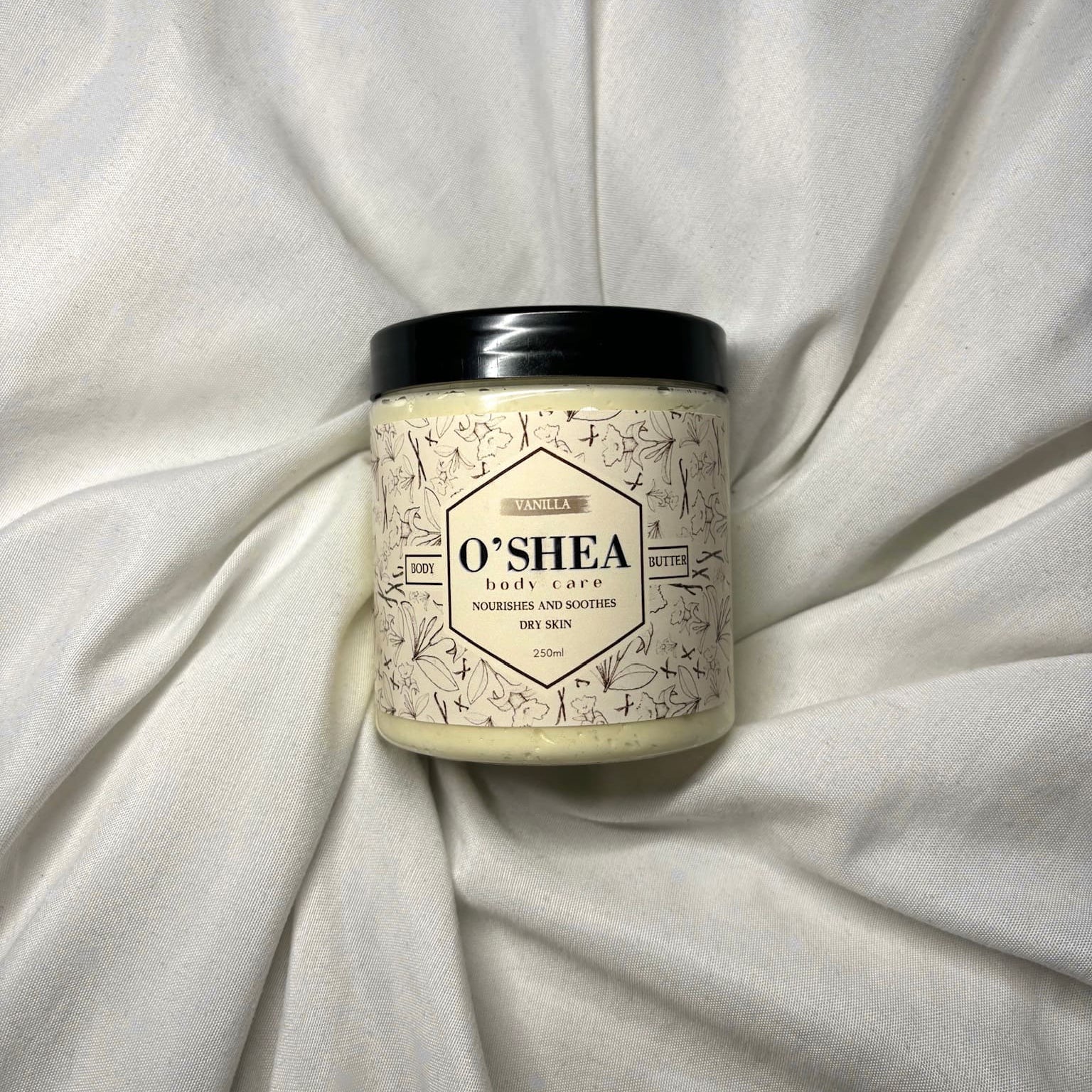 jar of vanilla organic shea body butter laid on a bed
